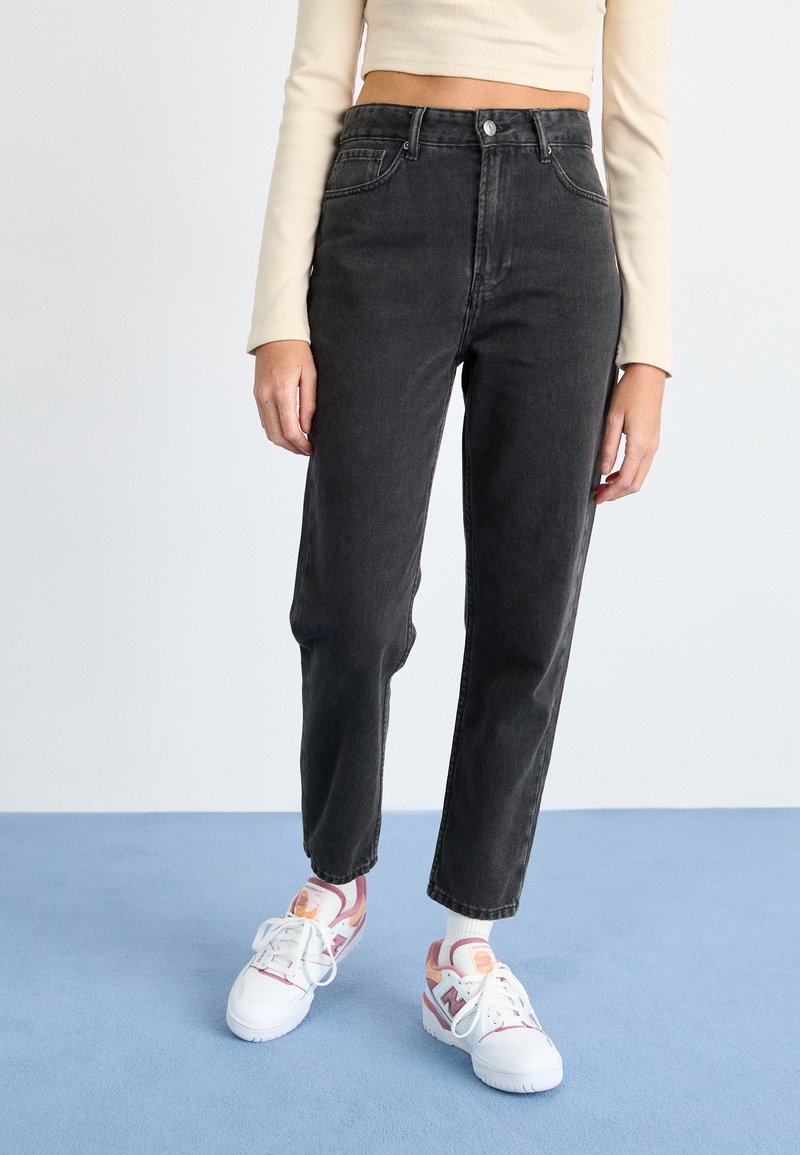 Čierne džíny so zvýšeným pásom a rovnými nohavicami, s piatimi vreckami a jemne vyblednutou textúrou, skombinované s farebnými teniskami.