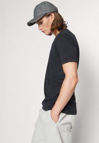 T-shirt preto de manga curta com decote redondo, combinado com um boné cinza de aba plana. O boné apresenta um tecido texturizado e detalhes de costura sutis.