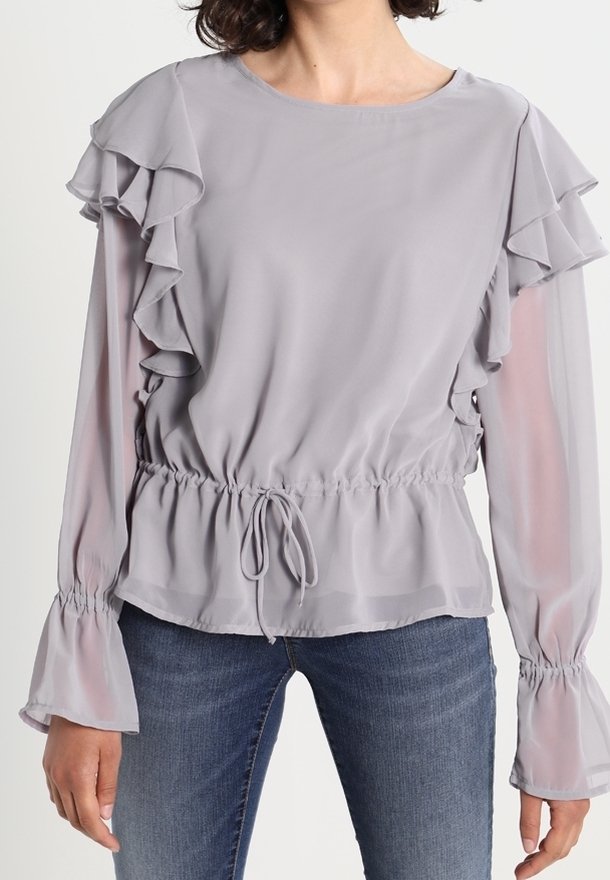 Blusa grigio chiaro con maniche a ruffle sovrapposte, vita elastica e dettaglio con cordoncino. Il tessuto semi-trasparente e le maniche a campana aggiungono texture.