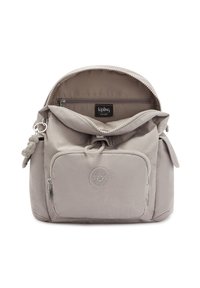 Mochila de tela gris claro con cierre de cremallera, bolsillo frontal y logotipo de goma. Presenta una forma redondeada y una superficie texturizada. Bolsillo interior visible.
