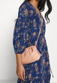 Sac en cuir rose avec un design froncé et une sangle ajustable, assorti à une robe bleu à imprimé floral avec des manches bouffantes.