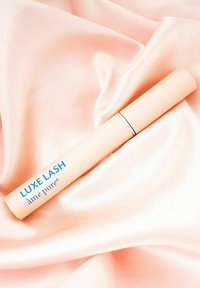 Luxe Lash mascara i ett matta mjukt rosa rör med blå bokstäver, vilande på en slät blekrosa satinbakgrund. Har en silverdetalj.