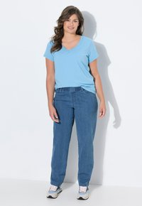 Camiseta de cuello en V azul claro, de corte holgado, combinada con pantalones estilo denim azul que tienen una cinturilla elástica. Modelo lleva zapatillas gris y blanco.