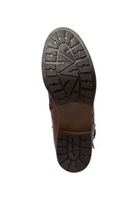 Brun lädersula med ett mönster av gropar, med spetsiga, vinklade former och en slät, mörkbrun häl.