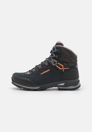 Mittellanger Wanderschuh aus dunkelblauem Wildleder mit grauen Akzenten. Verfügt über ein oranges Logo, ein Schnürsystem und eine strukturierte Gummisohle für besseren Halt.