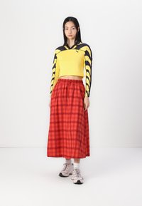Gul långärmad cropped top med svarta detaljer; röd rutig ankel-lång kjol med elastisk midja; ljusrosa sportskor.