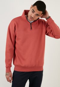 Fleece pullover in koraal met een hoge kraag en een halve rits. Voorzien van lange mouwen, een gestructureerd oppervlak en een aansluitende tailleband.