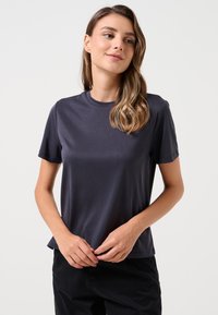 T-shirt grigio scuro a maniche corte in un tessuto morbido e elasticizzato; collo rotondo; vestibilità leggermente ampia; design minimalista senza motivi o accenti visibili.