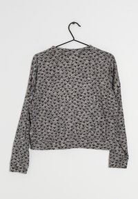 Gray long-sleeve top with black triangular pattern, made of soft fabric, featuring a crew neckline and relaxed fit, hanging from a black hook.
