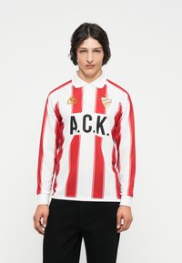 Červené a biele pruhované polo tričko s dlhým rukávom a golierom, s veľkým čiernym potlačou "A.C.K." a zlatými akcentmi loga Kappa.