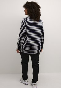 Navy and cream striped long-sleeve shirt with a rounded hem, paired with black pants and gray athletic shoes. Textured fabric, relaxed fit.