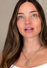 Collier en or avec un pendentif rectangulaire orné d'une pierre claire et d'un petit accent décoratif, porté avec un haut blanc.