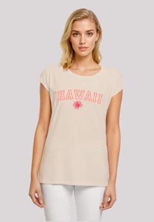 Beige cotton t-shirt with short sleeves, featuring the word "HAWAII" in red and a pink flower graphic below. Smooth texture, relaxed fit.