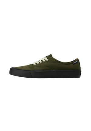 Zapatilla baja de lona verde oliva con cordones blancos y suela de goma negra, vista desde el lado exterior.