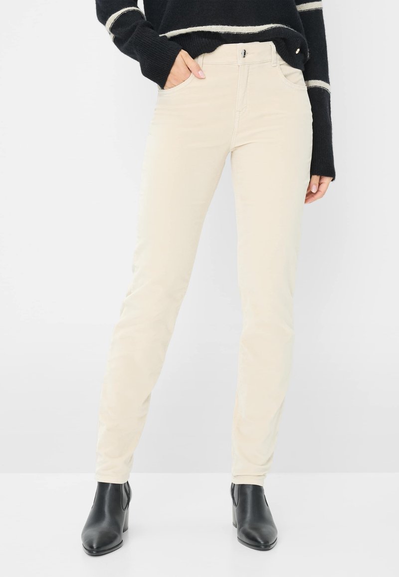 Beige slim-fit bukser lavet af bomuld med en glat tekstur, featuring frontlommer og lynlås-lukning, parret med sorte ankelstøvler.