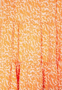 Orange klänning med en svävande design, med ett vitt abstrakt mönster. Den har lager av volanger och ett lätt, texturerat tyg.