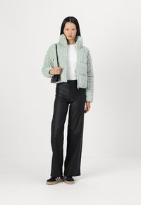 Veste puffer verte menthe avec un design court et une texture côtelée, associée à un pantalon noir taille haute et des chaussures noires.
