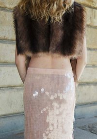 Boléro en fausse fourrure marron foncé avec un design court associé à une jupe rose clair à sequins présentant une texture multiple et un léger éclat.