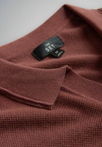 Chemise en maille texturée marron avec col plié et étiquette de taille noire indiquant "THE SET M" cousue à l'intérieur de l'encolure.