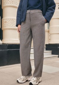 Brown and beige plaid trousers with a loose fit, featuring side pockets and a waistband. Paired with white sneakers with grey accents.