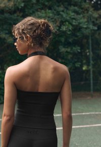 Top a fascia nero a costine e leggings coordinati a vita alta, texture liscia, design aderente, visti da dietro con uno sfondo verde scuro.