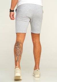 Graue Baumwollshorts mit elastischem Bund, kombiniert mit beigen Wildlederschuhen. Ein auffälliges Tattoo schmückt die Wade.