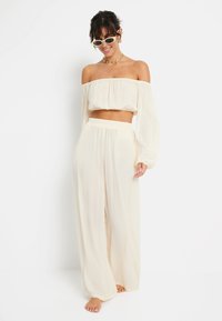 Kremna off-the-shoulder crop majica uparena s hlačama visokog struka širokih nogavica. Lagana, teksturirana tkanina s laganim krojem, minimalistički dizajn.