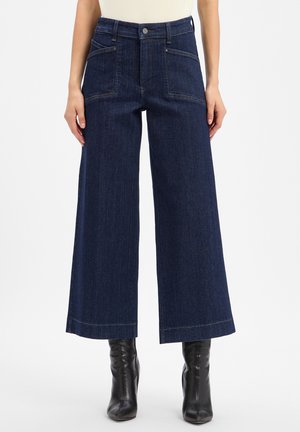 Dunkelblaue, weit geschnittene Cropped-Jeans mit vorderen aufgesetzten Taschen, Knopf- und Reißverschluss, getragen mit schwarzen, hochhackigen Stiefeletten.