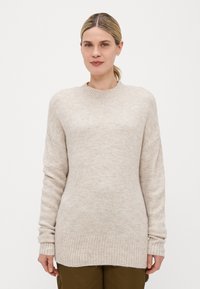 Beige strikkegenser med rund hals, ribbestrikkede mansjetter og kant, litt oversized passform og myk tekstur, vist på en modell.