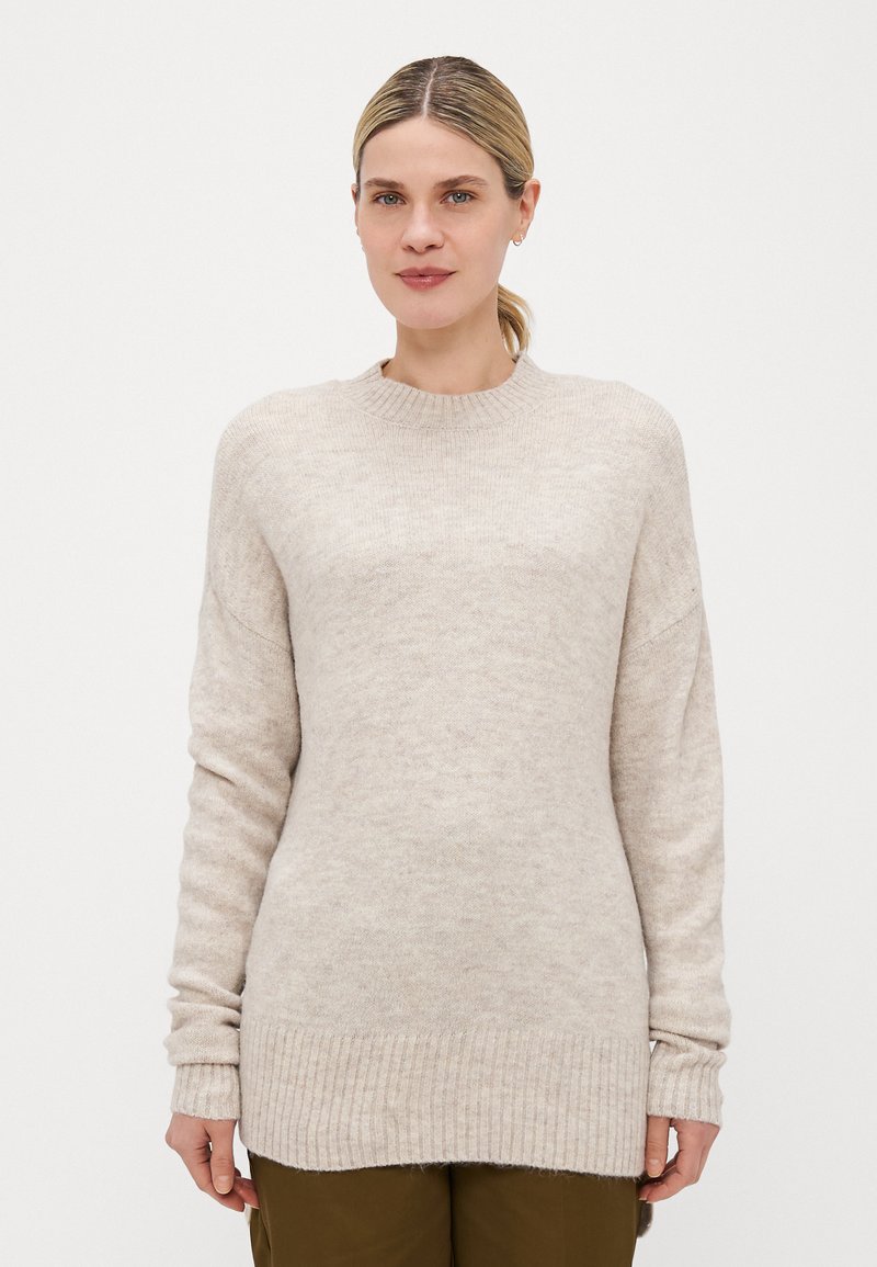 Pull en maille beige avec un col rond, des poignets et un ourlet côtelés, coupe légèrement oversize et texture douce, présenté sur un modèle.