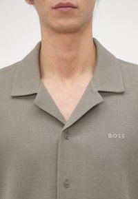Personne portant une chemise texturée gris clair à boutons avec col et "BOSS" brodée sur la poitrine.