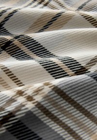 Soft fabric with a beige, black, and brown plaid pattern showing diagonal and horizontal stripes and textured weave details.