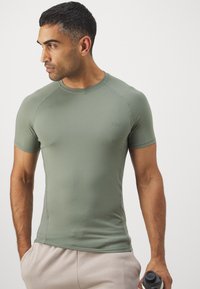 Pielāgota īsām piedurknēm sporta T-kreklu izsmalcinātā zaļā audumā ar apaļu apkakli un gludu tekstūru, ar izsmalcinātu logotipu uz krūtīm.