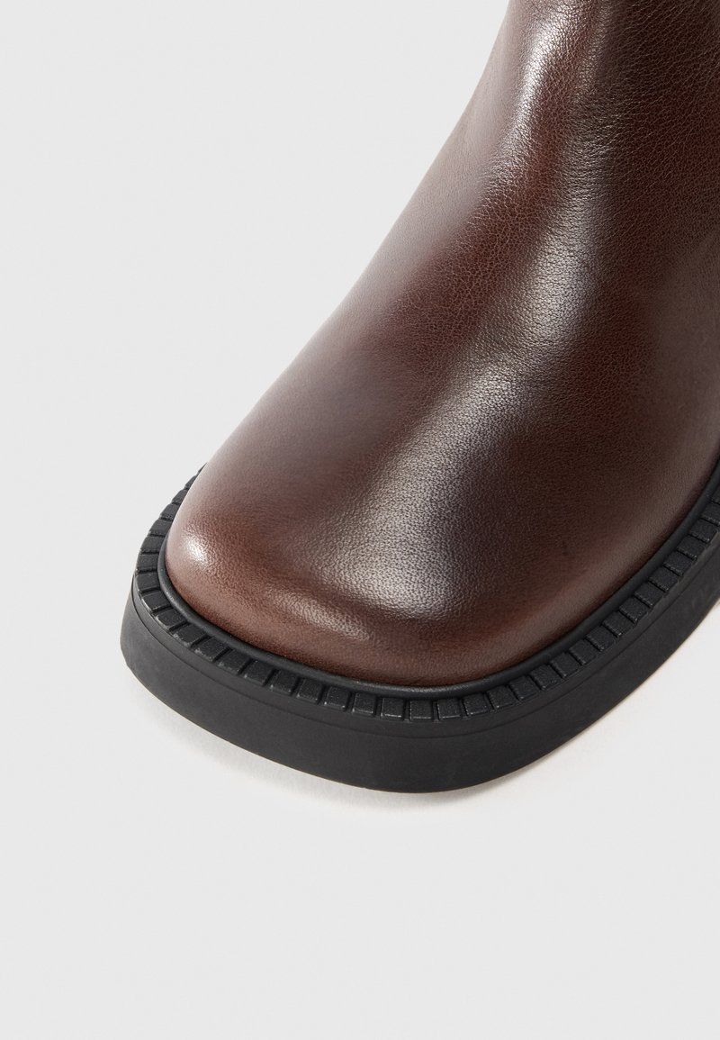 Bottines en cuir marron avec une finition lisse, bout arrondi et semelle en caoutchouc noir texturé à bord cannelé.