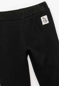 Sorte ribbede leggings med en glat talje og et lille firkantet mærke med blomstermotiv. En strækbar stof for komfort og pasform.