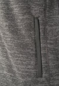 Tissu gris texturé avec un motif subtil, doté d'une poche d'accent noir verticale. Matière douce et tricotée, adaptée à une tenue décontractée.