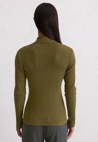 Olivengroene geribbelde blouse met lange mouwen en een getailleerd design en kraag. Heeft een gladde textuur en zijsplitten aan de zoom.