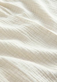 Tissu blanc texturé avec des plis subtils, mettant en avant un matériau doux et respirant, adapté pour l'habillement ou l'utilisation intérieure.