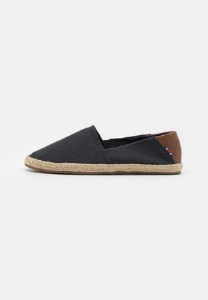 Espadrila sa tamnosivim platnenim gornjim dijelom, smešnim kožnim detaljem na peti i pletenom jutu kao potplatu. Bešavni dizajn, lagana tekstura.