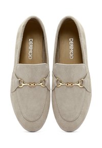 Mocassini in suede di un beige chiaro con una texture liscia, caratterizzati da un accento in catena dorata sulla parte anteriore. Suola piatta e design con punta arrotondata.