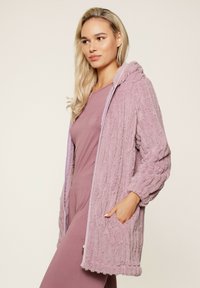 Cardigan con capucha de textura púrpura claro, con cierre de cremallera, patrón acanalado y bolsillos frontales; presenta un material suave y esponjoso.