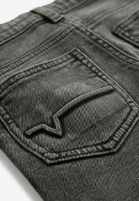 Jeans in denim grigio scuro con una singola tasca posteriore caratterizzata da un design cucito in rilievo. Il tessuto ha una finitura testurizzata e una leggera scoloritura.