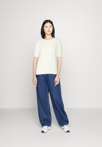 Grietos trumpomis rankovėmis megztas viršus su tekstūruotu raštu, derinamas su laisvomis mėlynomis džinsinėmis kelnėmis ir baltomis sportinėmis bateliais. Paprasta, laisva apranga.