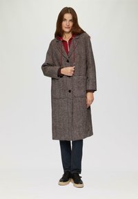 Houndstooth-patroon jas in bruin en crème, met een capuchon met rode trektouwen, front knopen en twee grote zakken.