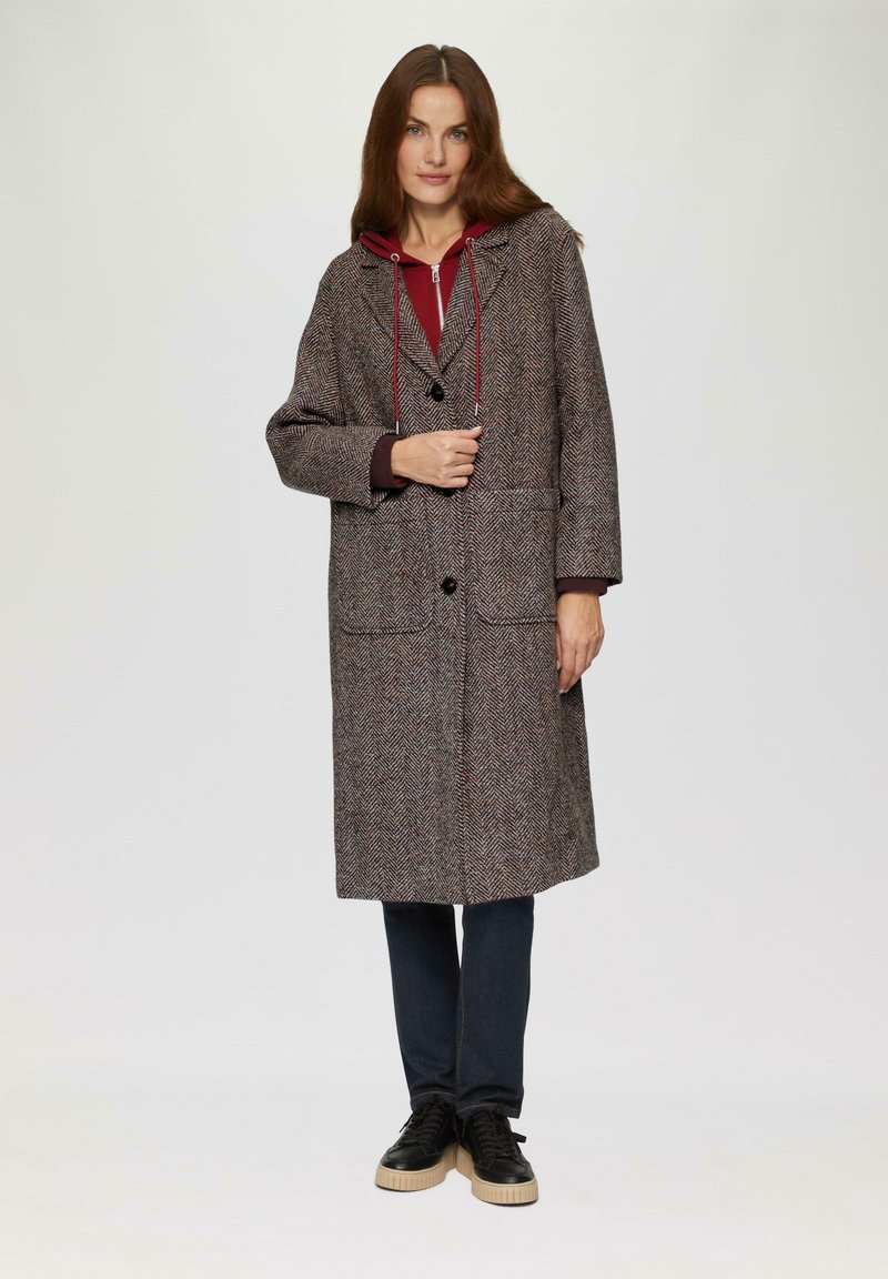 Houndstooth-patroon jas in bruin en crème, met een capuchon met rode trektouwen, front knopen en twee grote zakken.