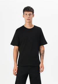 Sort kortærmet t-shirt lavet af bomuld med rund halsudskæring og løs pasform. Har en glat tekstur og ingen synlige mønstre eller logoer.