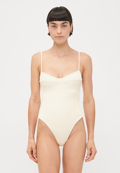 Geribbelde badmode in licht crème. Voorzien van dunne bandjes, een sweetheart halslijn en hoge uitsnijdingen bij de benen, die een slanke silhouet benadrukken.