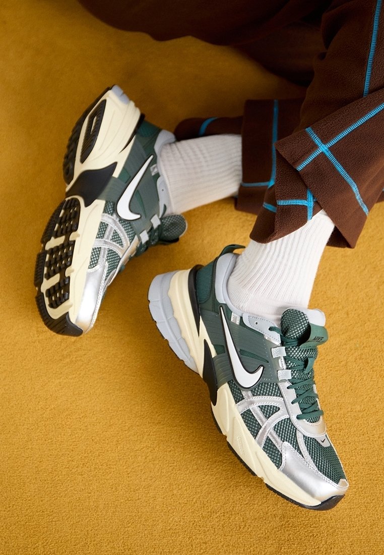 Gröna och silverfärgade sneakers med meshöverdel, svarta accenter och vit swoosh. Har en texturerad sula och snörningssystem, tillsammans med vita strumpor.