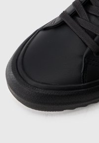 Μαύρο δερμάτινο αθλητικό παπούτσι με υφασμένη �μαύρη ελαστική σόλα, στρογγυλή μύτη και σκούρα κορδόνια, με λεία επιφάνεια και μινιμαλιστικές λεπτομέρειες σχεδίασης.