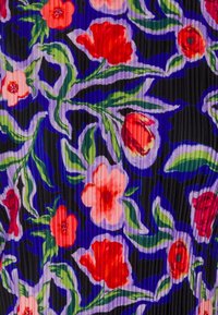 Tissu coloré avec des fleurs rouges et roses, des feuilles vertes et des contours violets sur un fond plissé texturé bleu foncé.